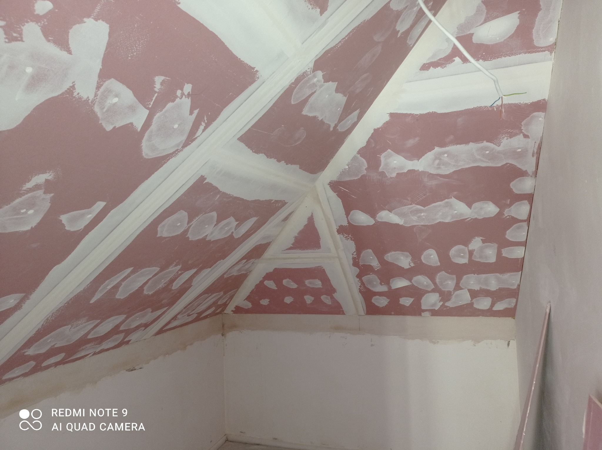 Skośny sufit poddasza z płyt kartonowo-gipsowych, wstępnie zagruntowany i z widocznymi spoinami oraz miejscami nałożoną gładzią w plamy, przygotowany do dalszych prac wykończeniowych.