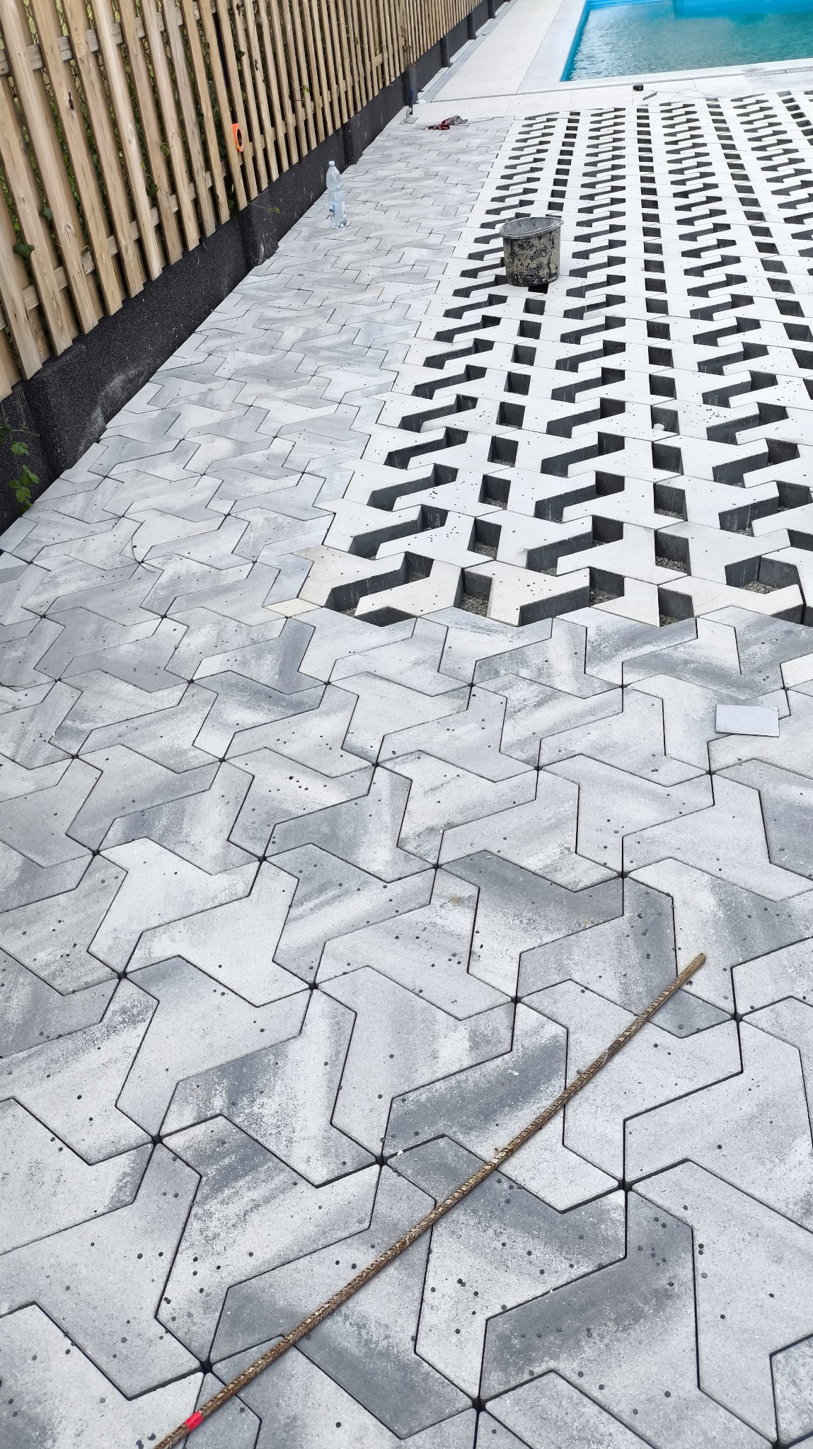 Układanie ażurowej kostki brukowej w Gdowie, widok z góry. Częściowo ułożona nawierzchnia z szarej kostki obok basenu i drewnianego ogrodzenia.