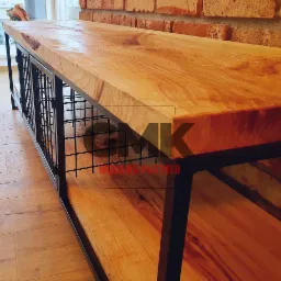 Stolik kawowy z blatem z litego drewna i metalową konstrukcją z siatki, ustawiony na drewnianej podłodze przy ceglanej ścianie.