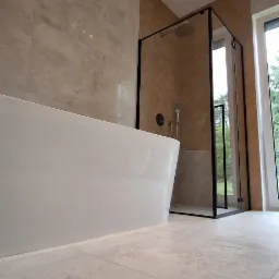 Nowoczesna łazienka z wolnostojącą wanną i kabiną prysznicową typu walk-in, wykończona płytkami w odcieniach beżu i szarości. Minimalistyczny design, oświetlenie punktowe.