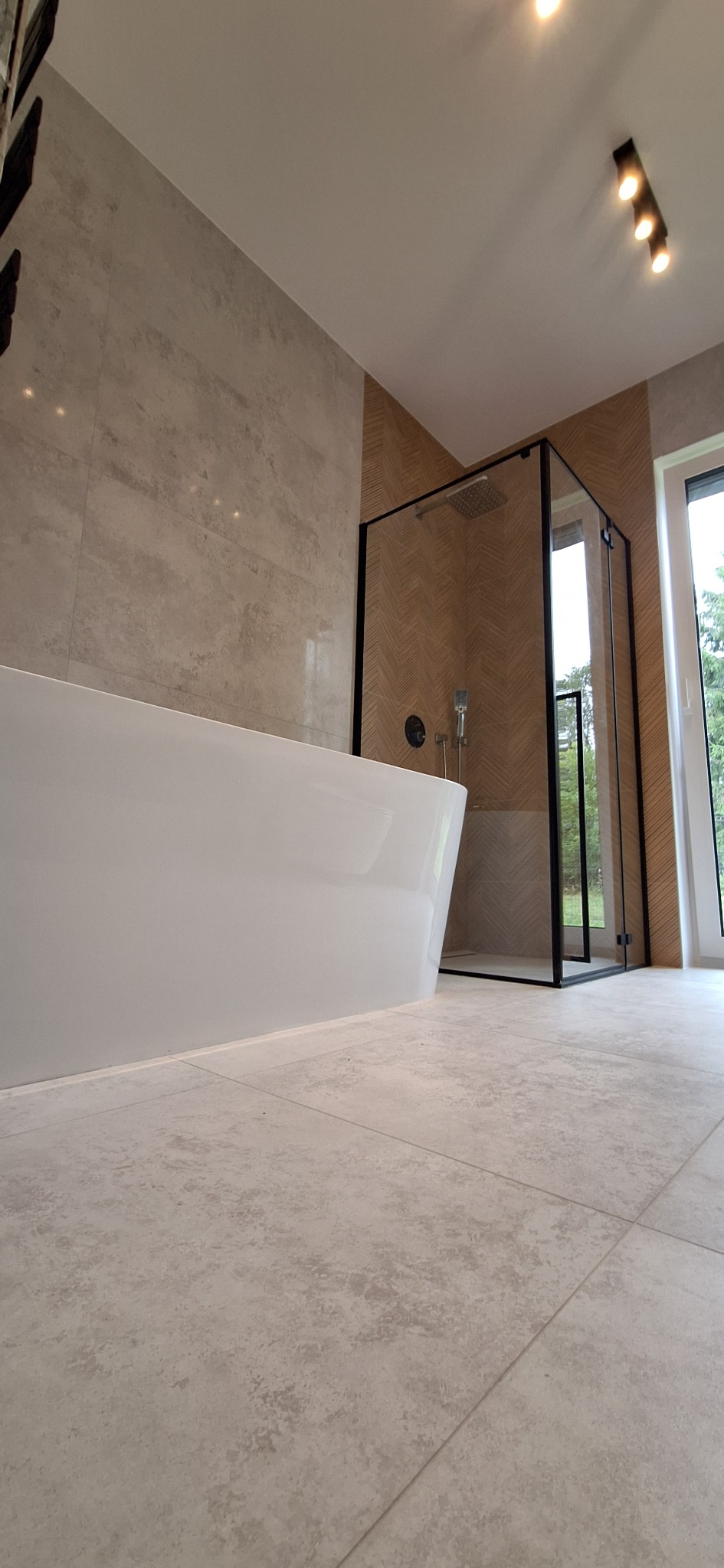 Nowoczesna łazienka z wolnostojącą wanną i kabiną prysznicową typu walk-in, wykończona płytkami w odcieniach beżu i szarości. Minimalistyczny design, oświetlenie punktowe.
