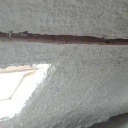 Poddasze z oknem dachowym pokryte grubą warstwą białej pianki PUR, widoczne drewniane elementy konstrukcyjne