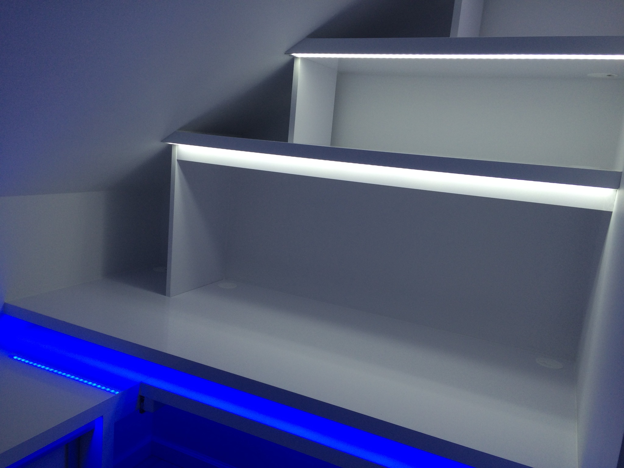 Biała zabudowa pod skosem ze schowkami i podświetleniem LED w kolorze białym i niebieskim.