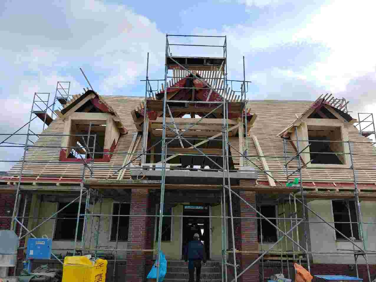 Dom w trakcie budowy dachu z widocznymi oknami dachowymi i rusztowaniami, częściowo pokryty dachówką.