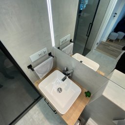 Platan construction - Nowoczesna łazienka we Wrocławiu po remoncie: kwadratowa umywalka nablatowa z chromowaną baterią, drewniany blat, szara ściana z podświetlanym lustrem i czarnymi akcentami, widoczny fragment kabiny...