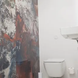 Nowoczesna łazienka z wiszącą toaletą, umywalką i ścianą wyłożoną płytkami imitującymi marmur w odcieniach brązu, szarości i bieli.