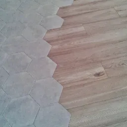 Połączenie podłogi z paneli imitujących drewno i szarych, sześciokątnych płytek ceramicznych, tworzące ciekawy wzór.