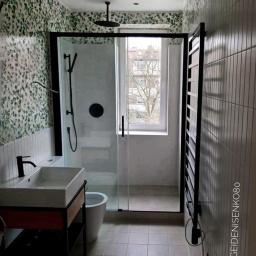 Remonty mieszkań Wrocław - Nowoczesna łazienka we Wrocławiu z kabiną prysznicową typu walk-in z czarnymi ramami, umywalką nablatową na metalowym stelażu z drewnianą półką i grzejnikiem drabinkowym w kolorze czarnym,...