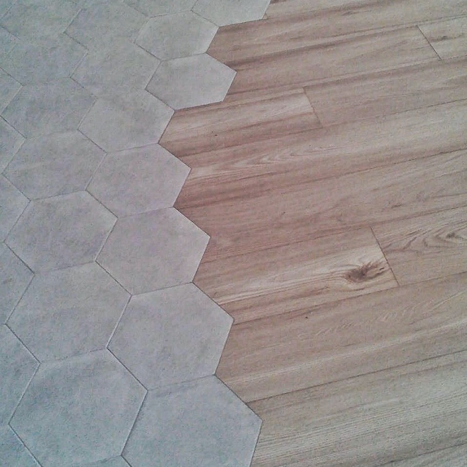 Połączenie podłogi z paneli imitujących drewno i szarych, sześciokątnych płytek ceramicznych, tworzące ciekawy wzór.