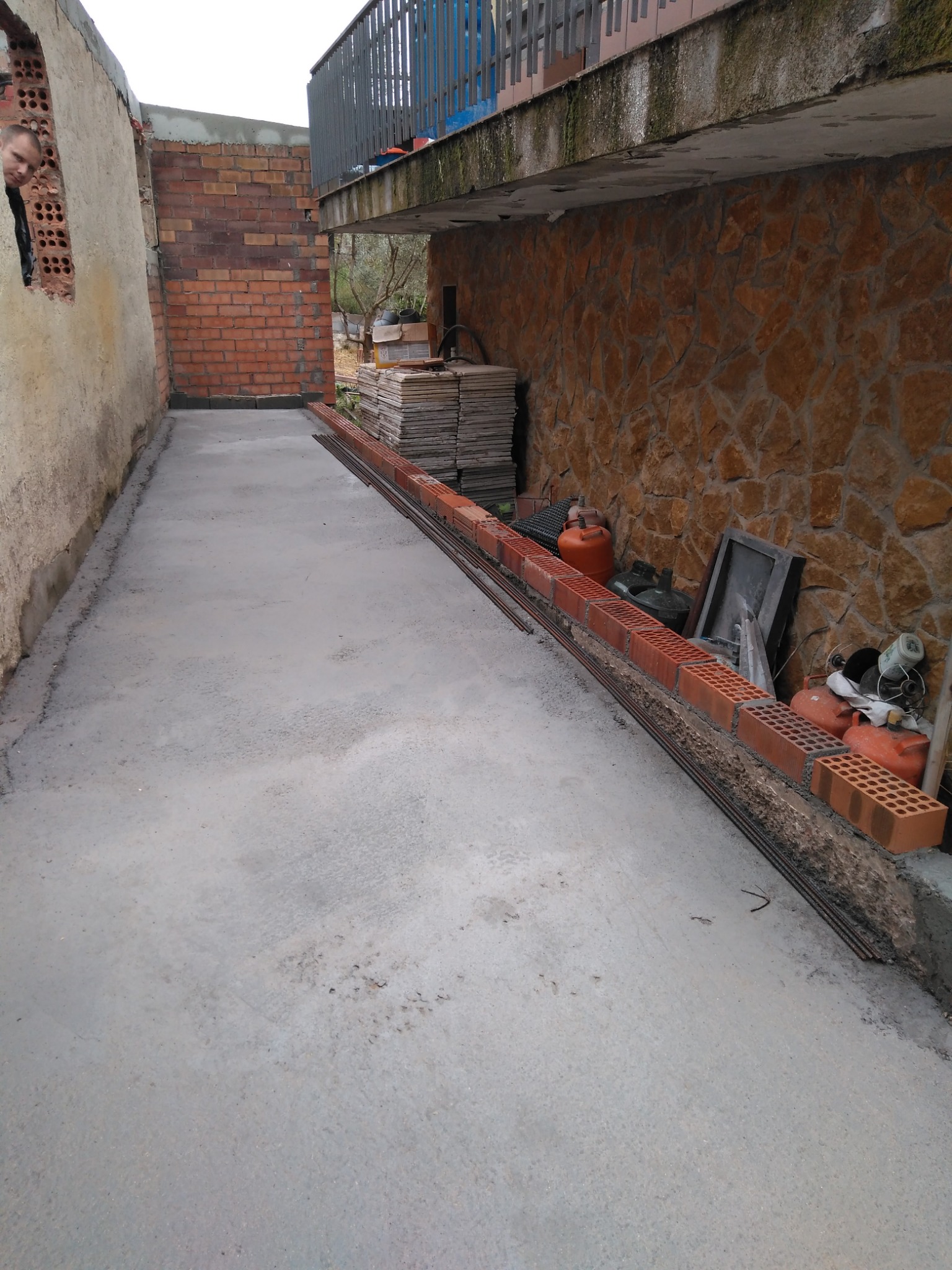 Przygotowany betonowy podkład pod rozbudowę domu w Manresie, widoczne cegły klinkierowe i pręty zbrojeniowe przygotowane do dalszych prac murarskich, w tle ściana z kamienia naturalnego.