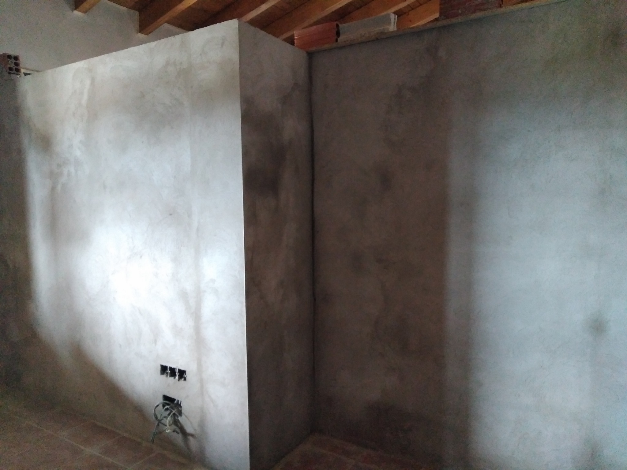 Surowe ściany w rogu pomieszczenia, świeżo pokryte szpachlą, z widocznymi puszkami elektrycznymi i przewodami, przygotowane do dalszych prac wykończeniowych.