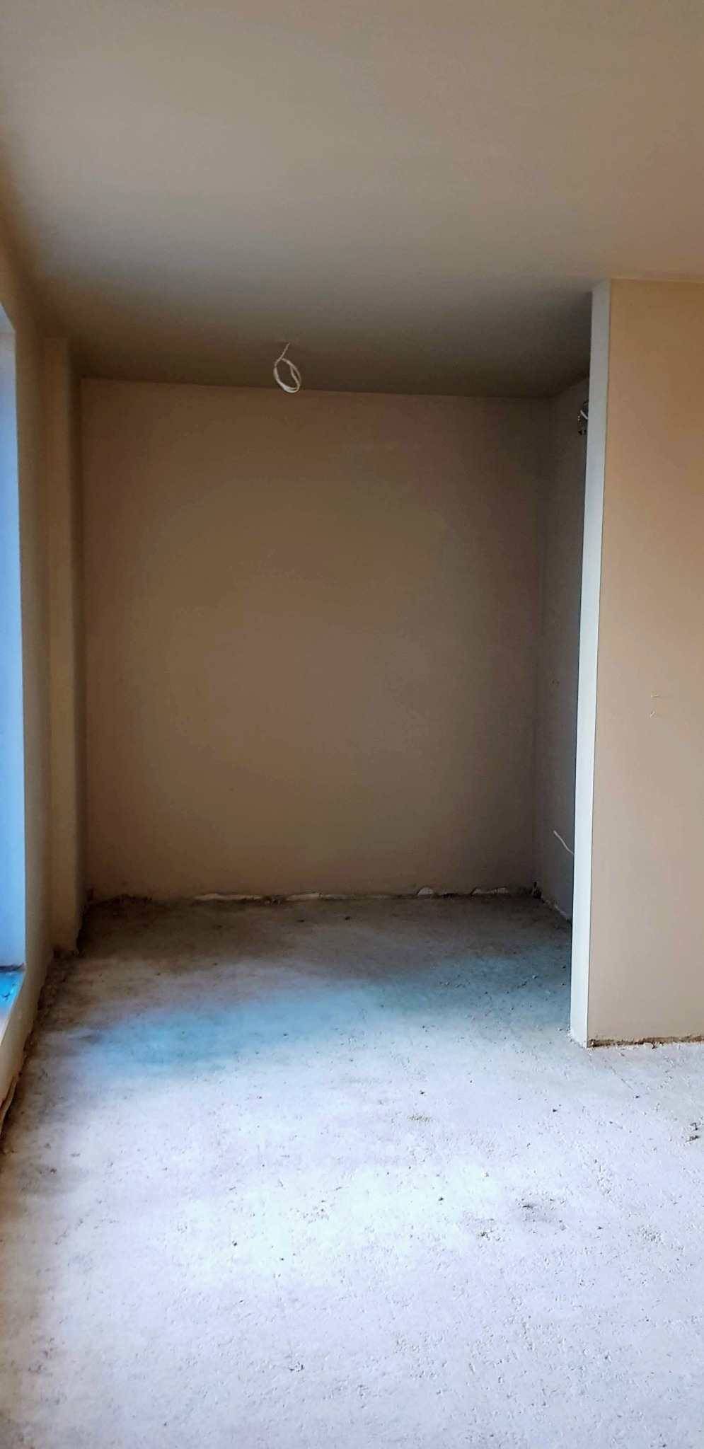 Wnętrze pokoju po tynkowaniu maszynowym ścian i sufitu, widoczne wystające przewody elektryczne i surowa posadzka przed wylewką.