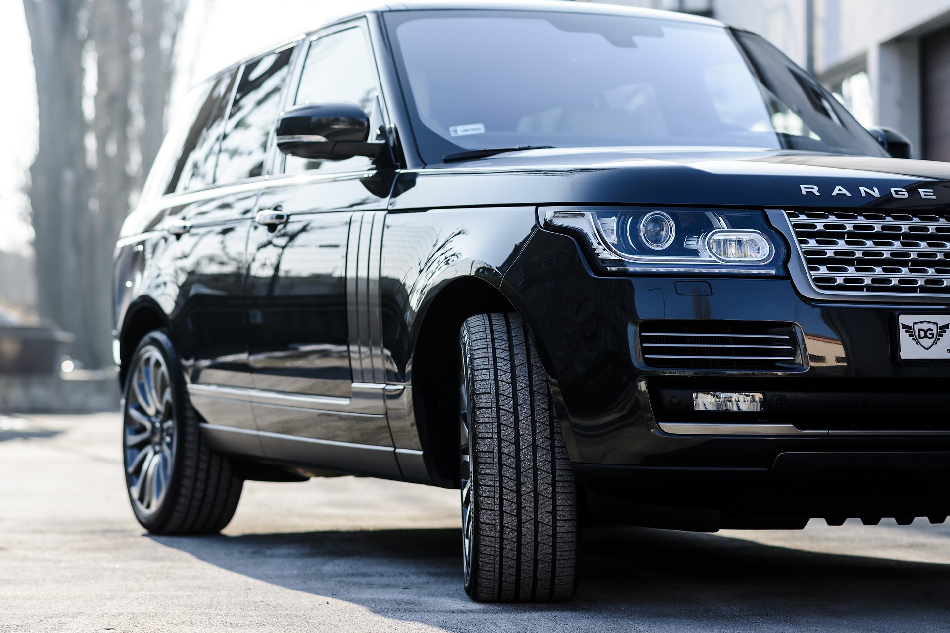 Czarny Range Rover z widoczną przednią oponą, chromowanym grillem i reflektorami LED, zaparkowany na betonowym podłożu z delikatnym rozmyciem tła.
