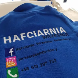 Niebieska koszulka polo z wyhaftowanym logo firmy 'Hafciarnia Września' wraz z ikonami Facebooka, Instagrama i numerem telefonu.