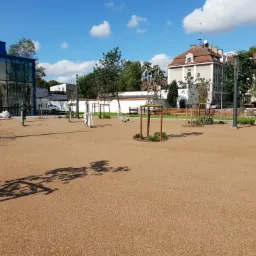 Nowo wykończony plac miejski w Słupsku z beżową, drobną nawierzchnią, młodymi drzewkami i elementami siłowni zewnętrznej, widok w słoneczny dzień.