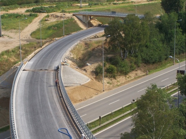 Nowa droga w budowie, widok z góry, z widocznym fragmentem mostu, pracownikami przy krawędzi i niebieskim wężem na jezdni.