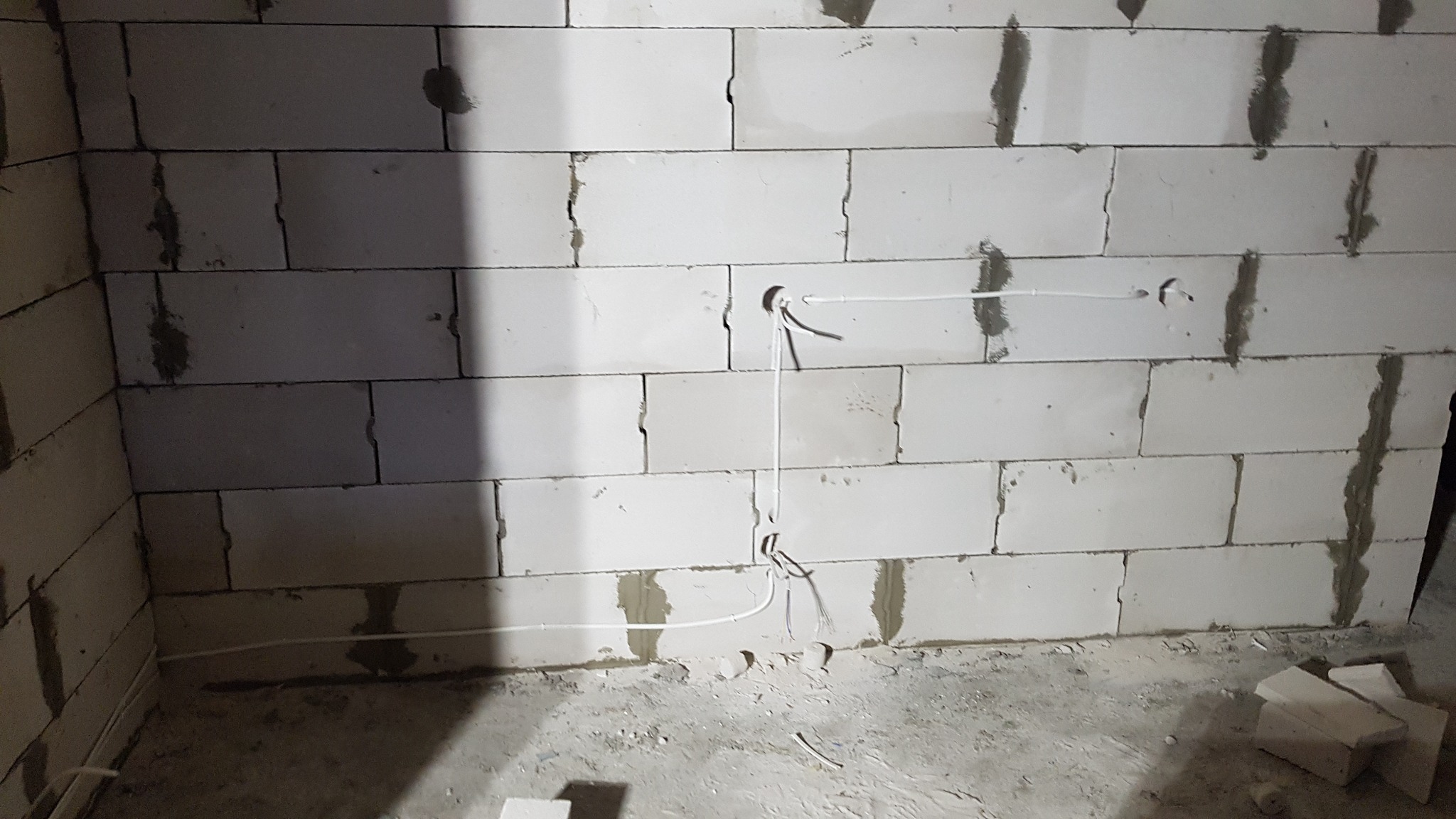 Ściana z betonu komórkowego w trakcie montażu przewodów elektrycznych, widoczne otwory i wystające kable.