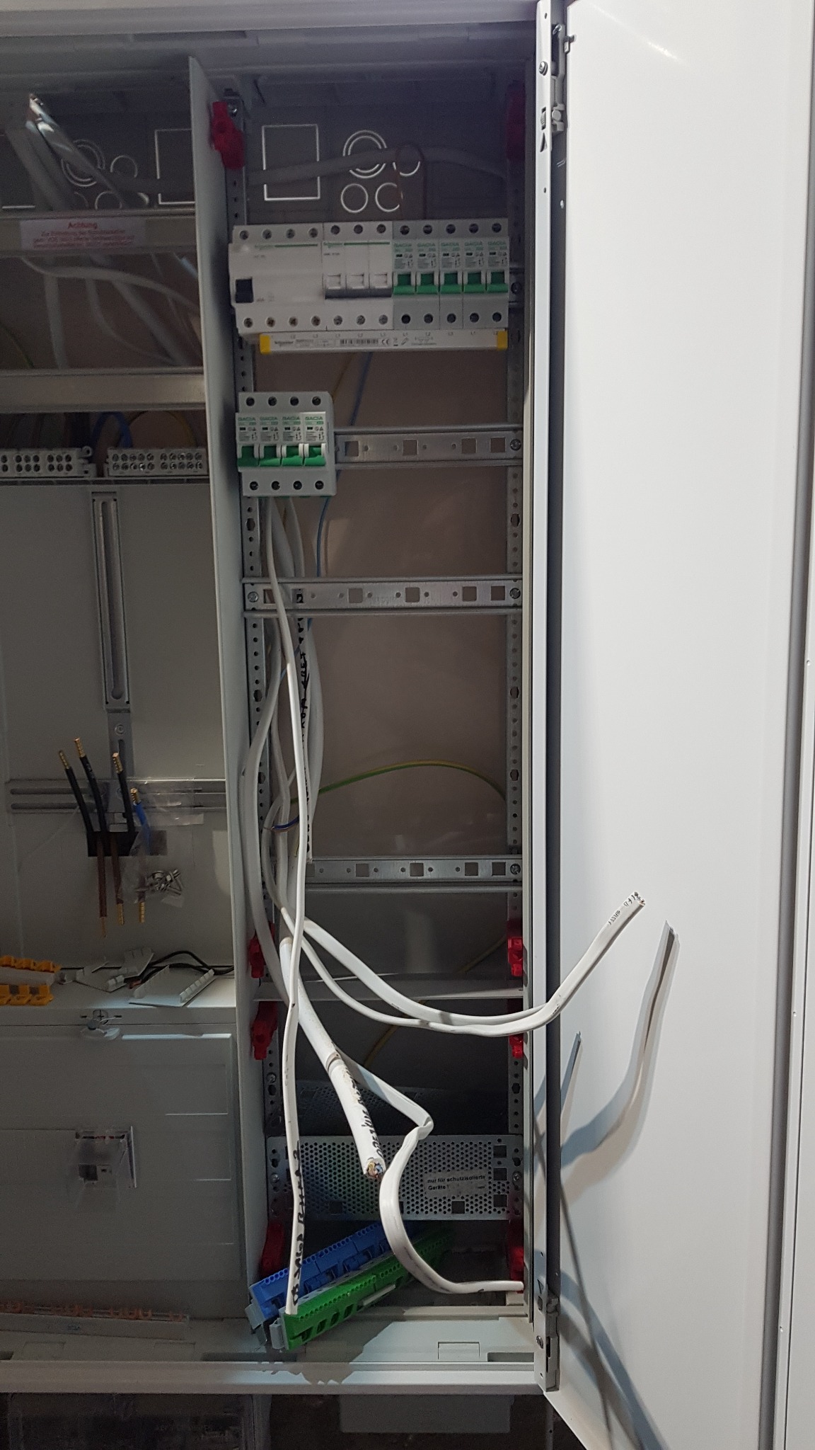 Otwarta szafa rozdzielcza w trakcie montażu, widoczne zabezpieczenia różnicowoprądowe, przewody elektryczne, listwy montażowe i elementy przyłączeniowe.