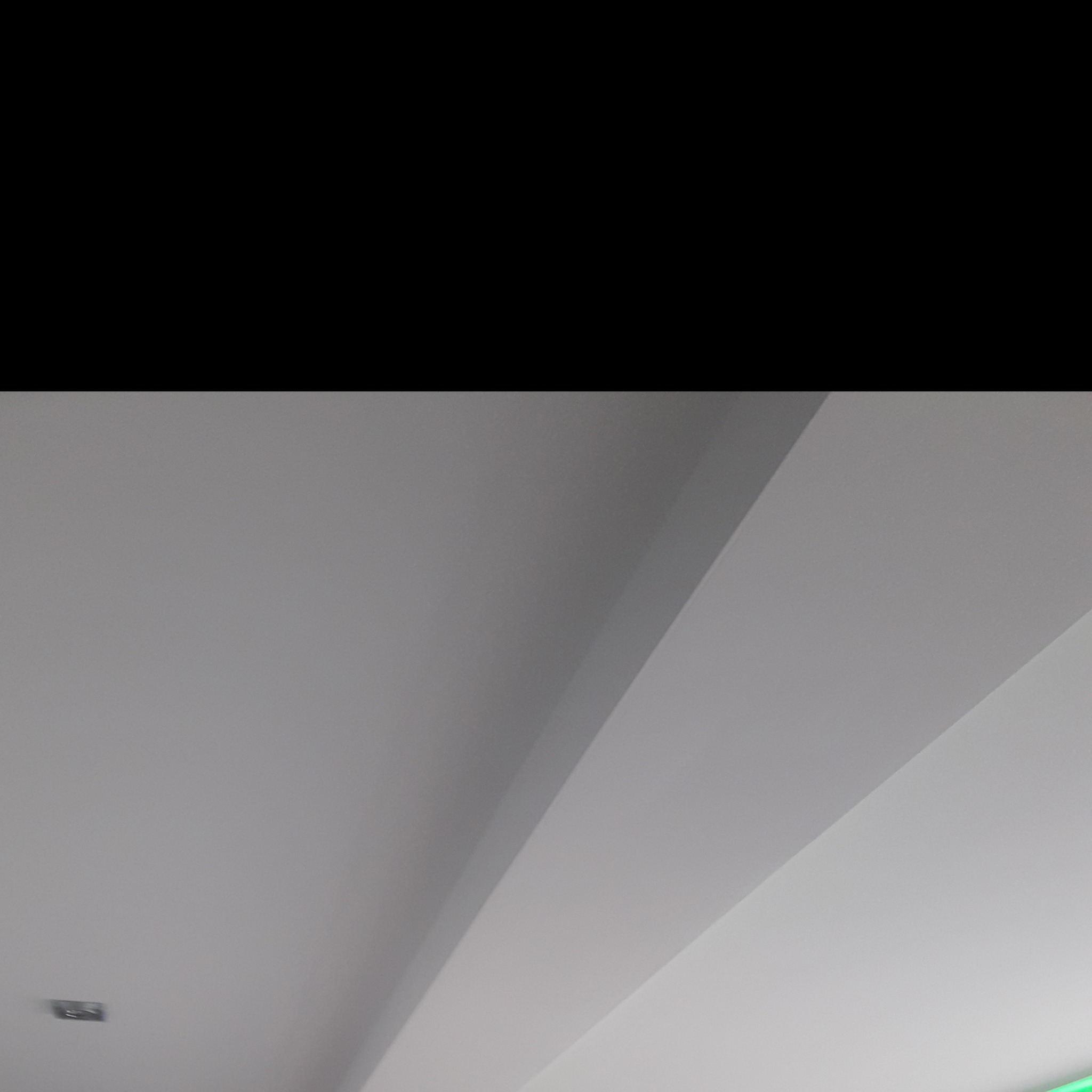 Fragment białego sufitu z widocznymi liniami podziału i małym, kwadratowym elementem oświetleniowym.