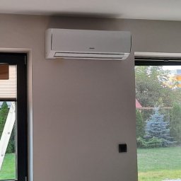 Ergo-klima Tomasz Menzel - Zamontowany klimatyzator ścienny w jasnym pomieszczeniu z widokiem na ogród przez okno, widoczny fragment drabiny oparty o ścianę.