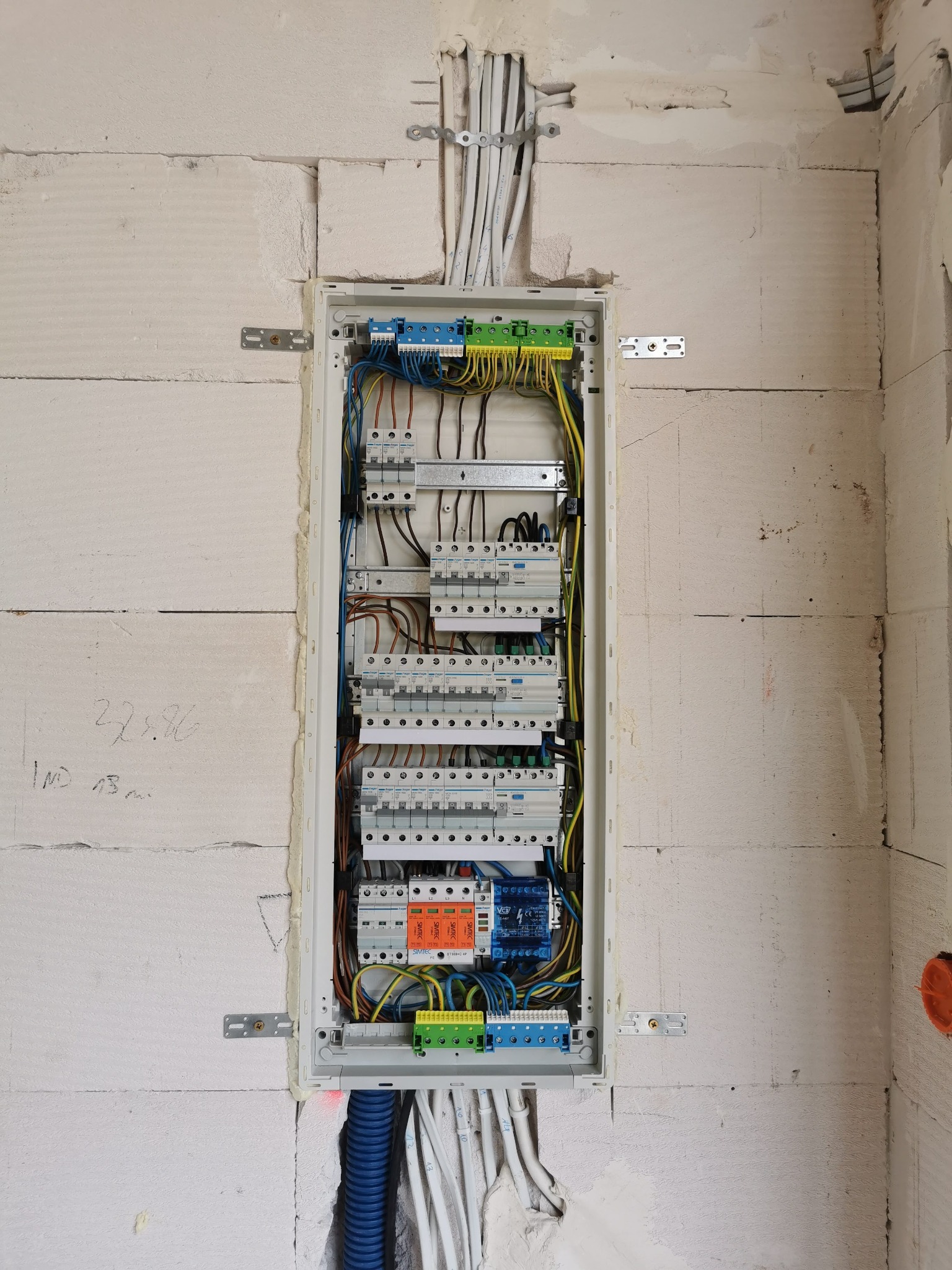 Rozdzielnica elektryczna z zabezpieczeniami różnicowoprądowymi i nadprądowymi, zamontowana w surowej ścianie z betonu komórkowego, widoczne kable i peszel doprowadzone do skrzynki.