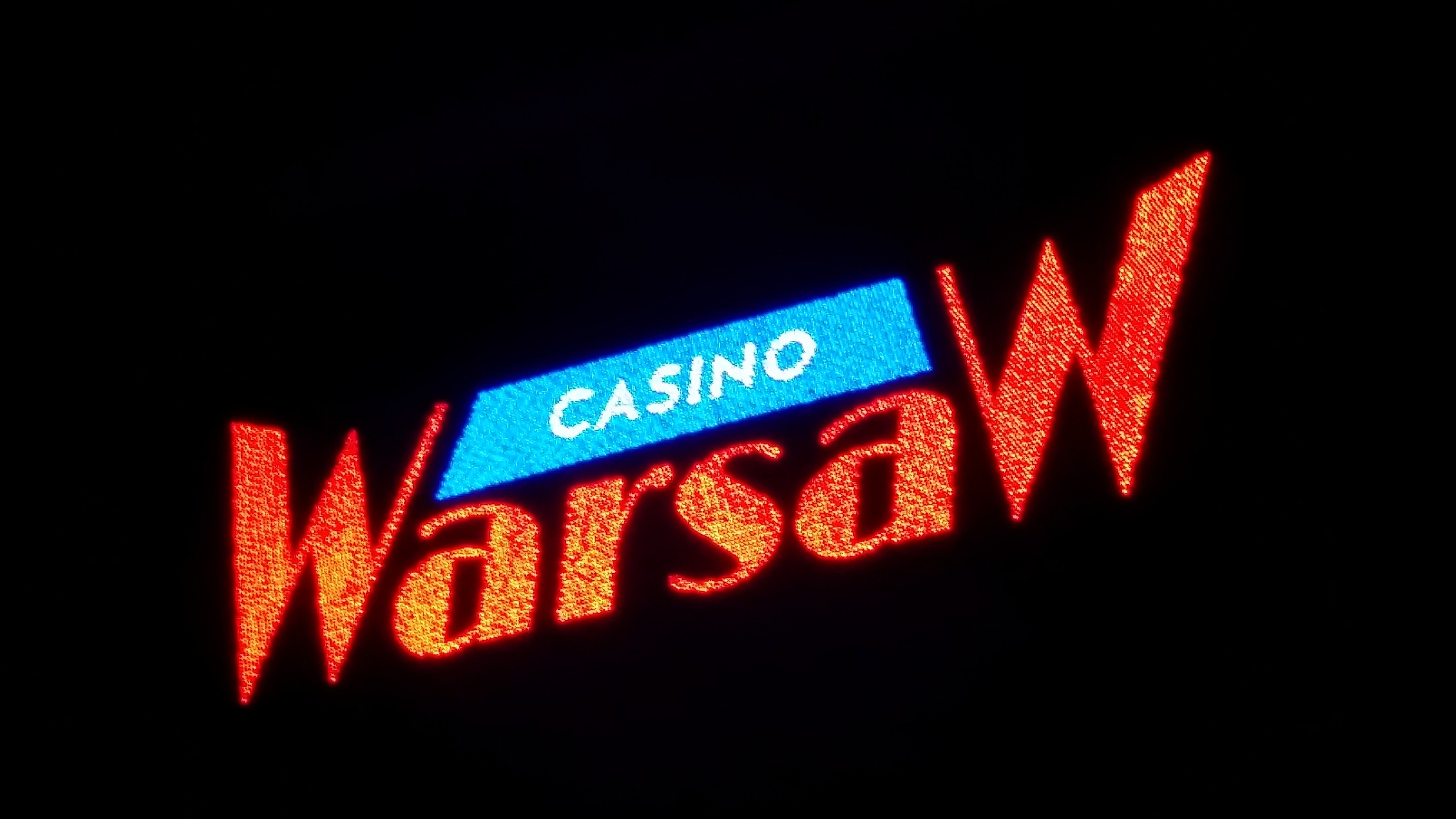 Neonowy szyld z napisem CASINO WarsaW, podświetlony na czerwono i niebiesko, widoczny w ciemności.