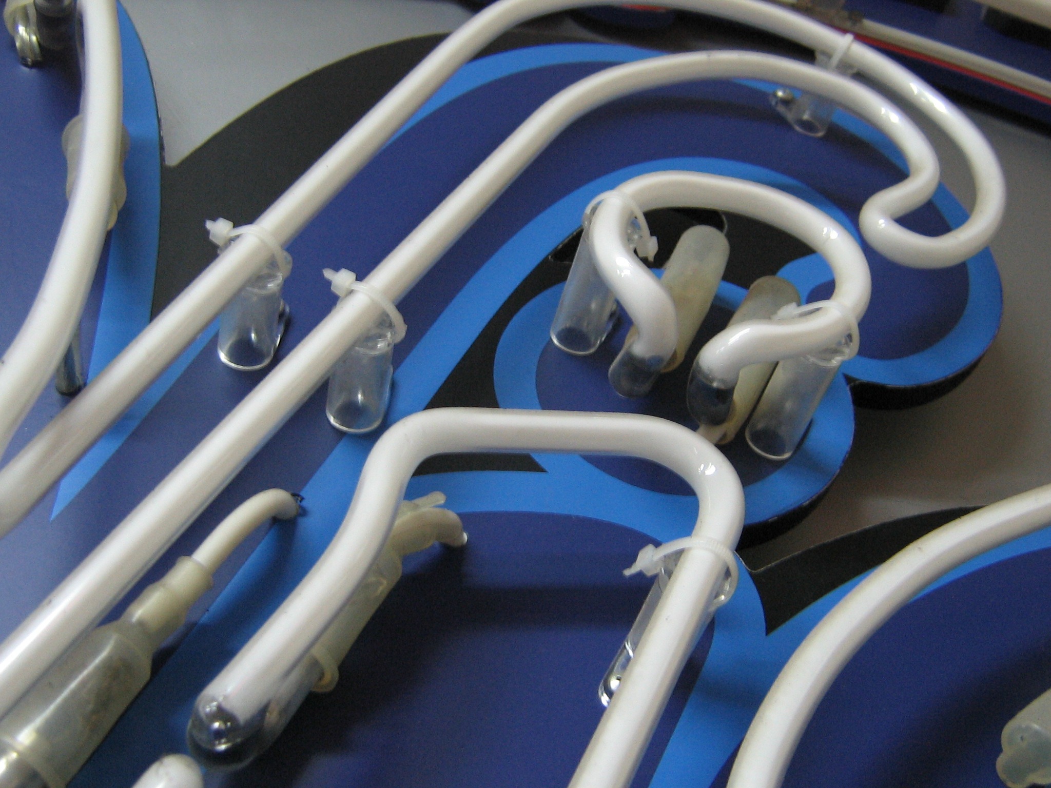 Detaliczny widok białych rurek neonowych przymocowanych do niebieskiego i czarnego podłoża za pomocą przezroczystych uchwytów i opasek zaciskowych.