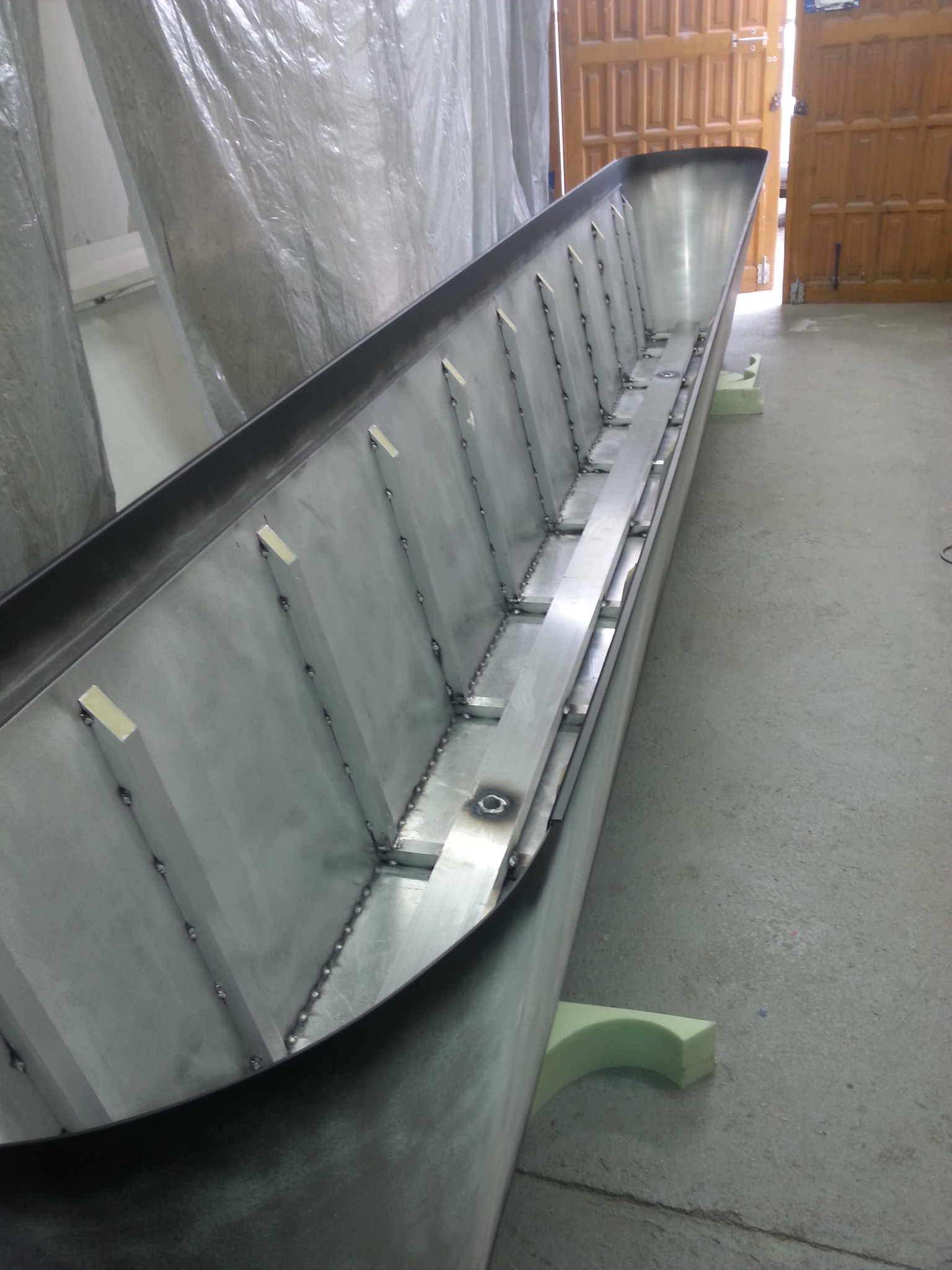 Wnętrze długiego, metalowego koryta z przyspawanymi wzmocnieniami, stojącego na piankowych podporach, widoczne ślady spawania