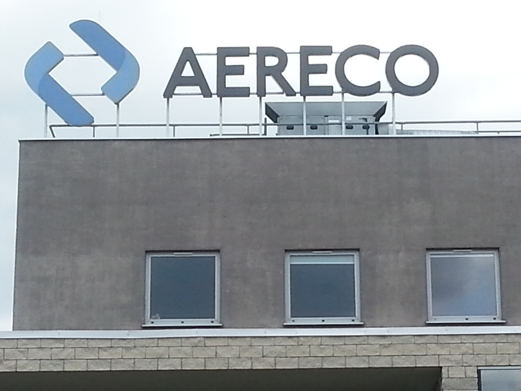 Budynek biurowy z logo AERECO na dachu, widoczne trzy okna i fragment muru z cegieł