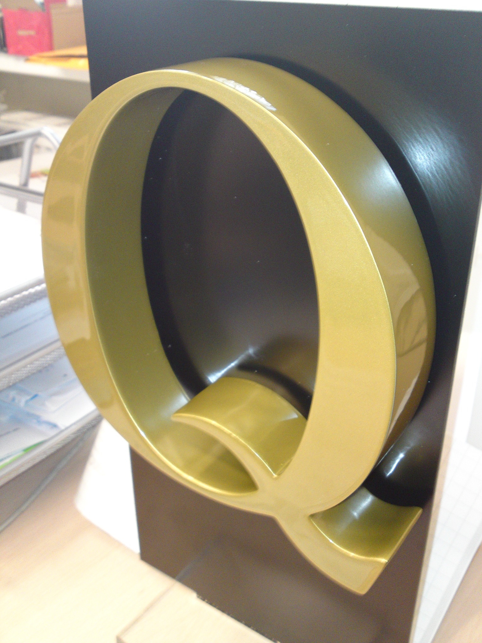 Złota, przestrzenna litera Q na czarnym tle, potencjalny element identyfikacji wizualnej firmy.