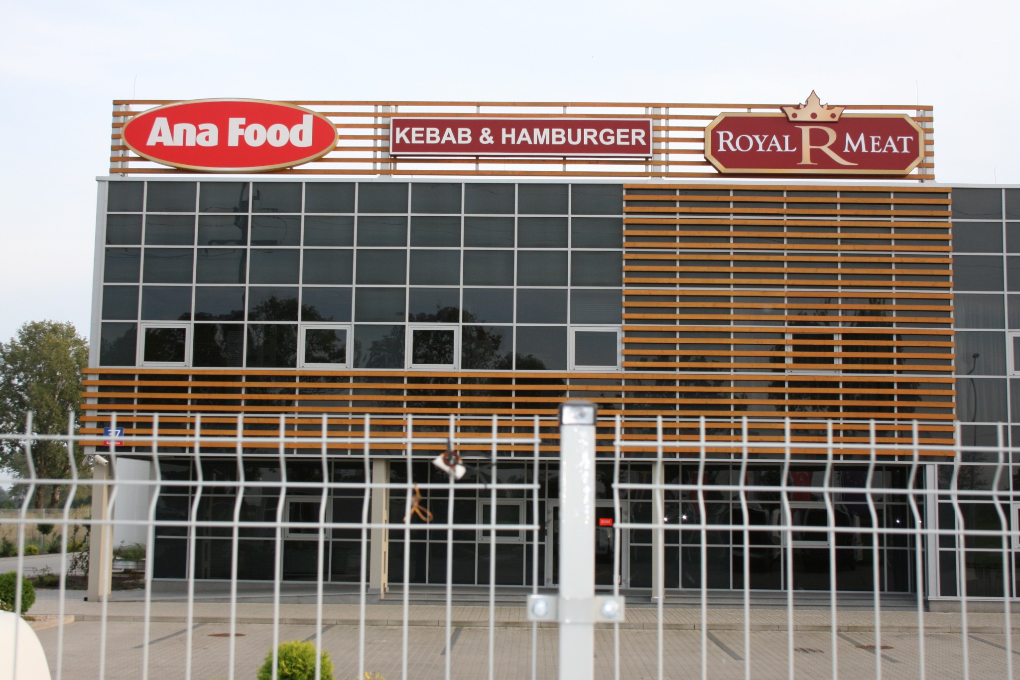 Budynek restauracji z dużymi szyldami reklamowymi na dachu, widok zza metalowego ogrodzenia.