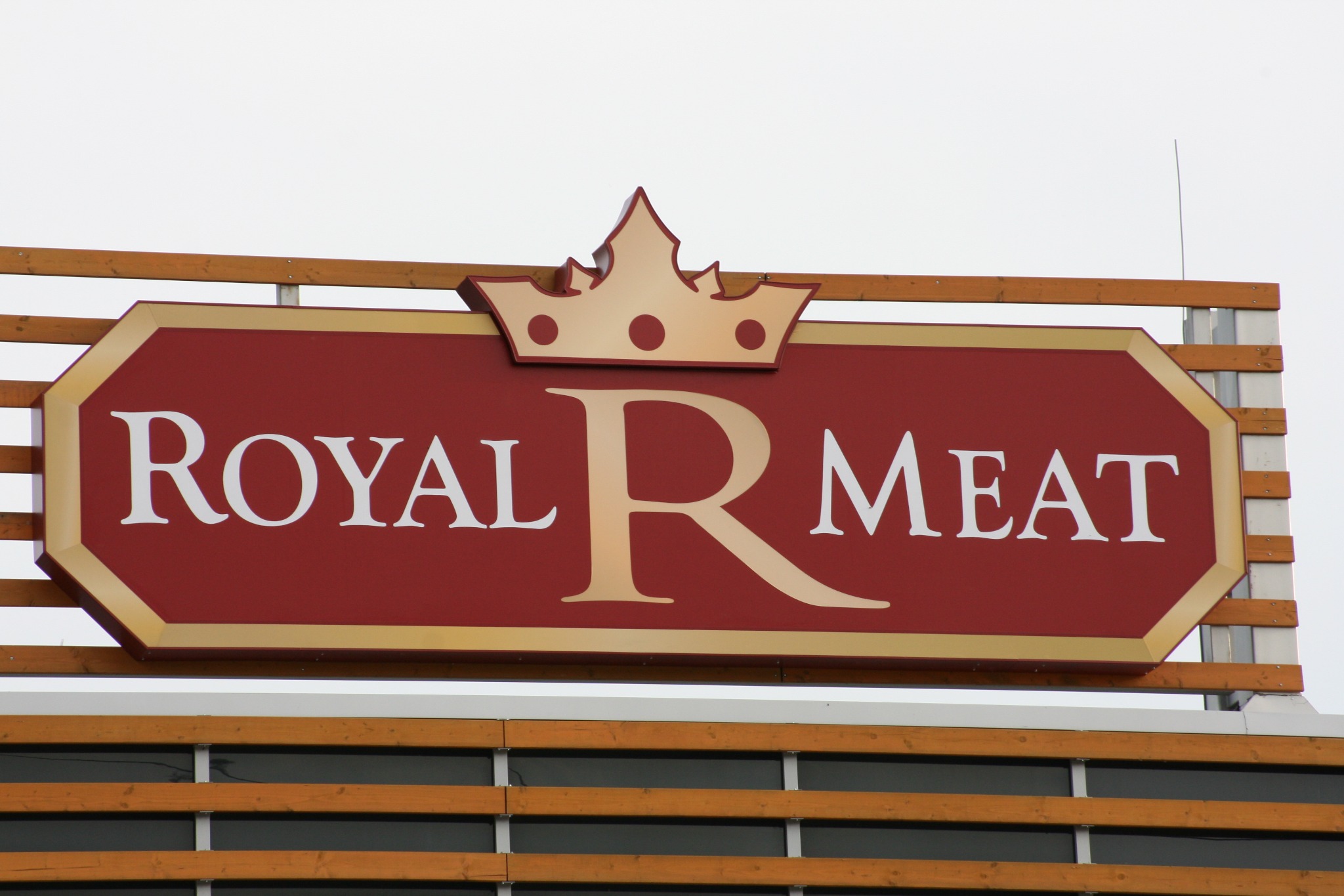 Szyld reklamowy z napisem 'ROYAL MEAT' w kolorze białym i złotym, zwieńczony koroną, zamontowany na budynku w Dziekanowie Polskim.