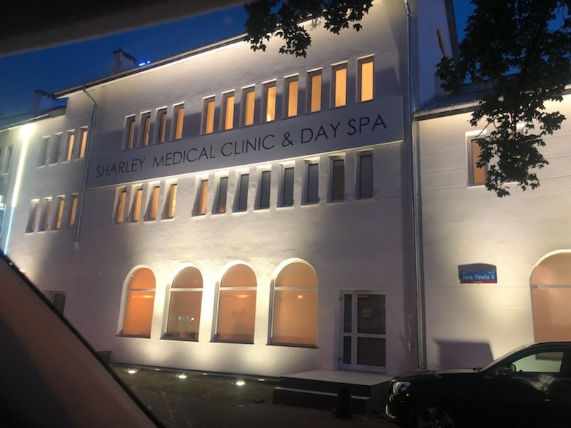 Elewacja budynku Sharley Medical Clinic & Day Spa oświetlona wieczorem, z widocznymi oknami i nazwą kliniki na fasadzie.