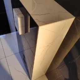 Nowoczesna wyspa kuchenna z białego marmuru z czarnymi akcentami, widok z góry na błyszczące płytki podłogowe, wiązka kabli na blacie.