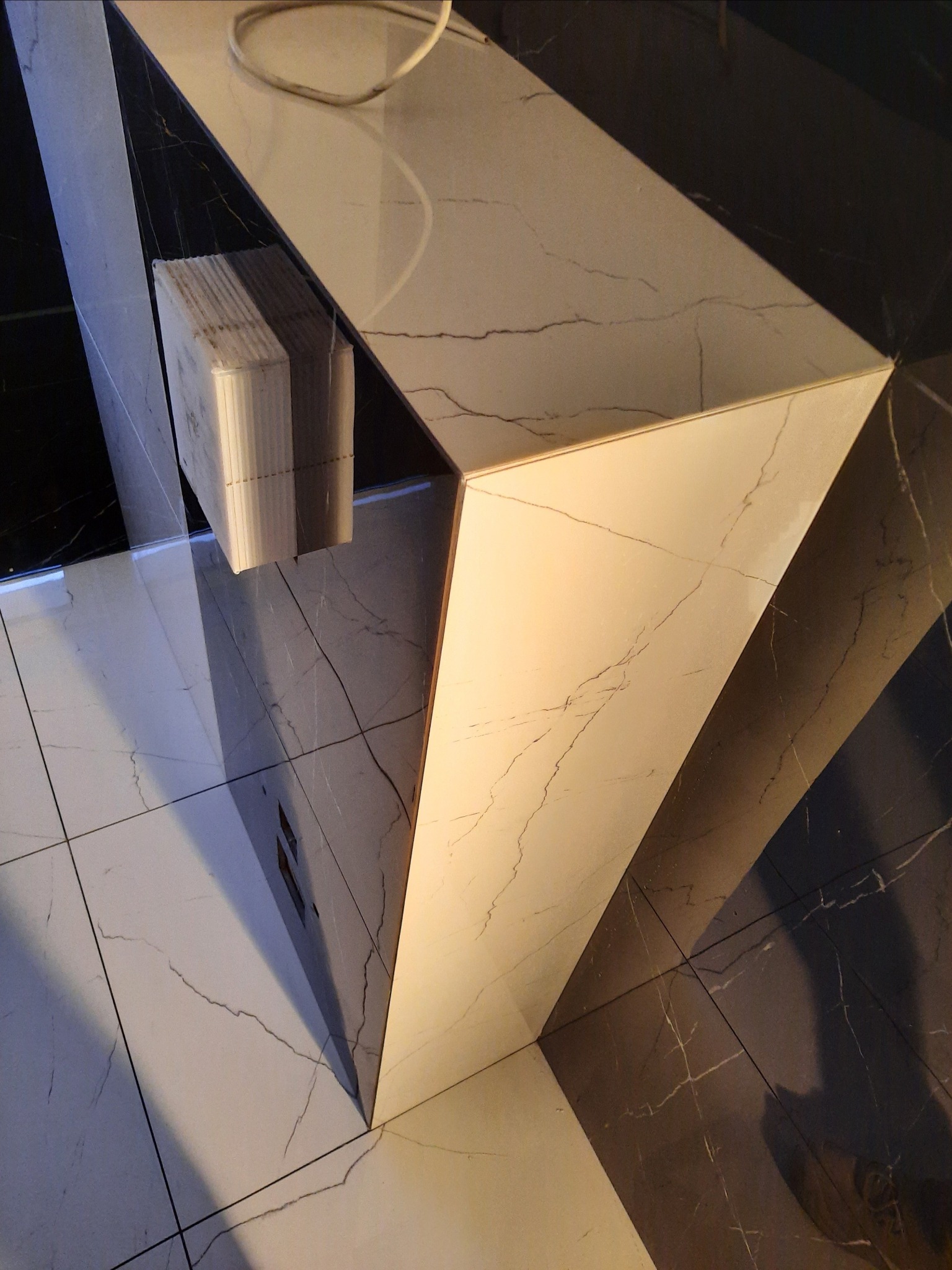 Nowoczesna wyspa kuchenna z białego marmuru z czarnymi akcentami, widok z góry na błyszczące płytki podłogowe, wiązka kabli na blacie.