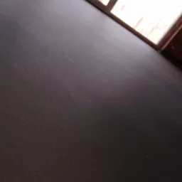 Gładka, ciemnoszara posadzka w słonecznym pokoju, widok z niskiego kąta w kierunku okna.