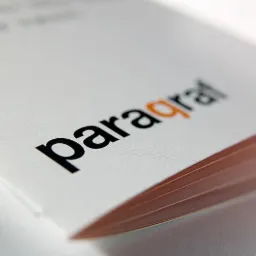 Biała broszura z czarno-pomarańczowym logo 'paragraf', widoczne krawędzie kartek, delikatny wzór w tle.