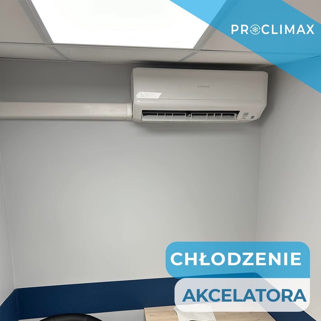 Biały klimatyzator Mitsubishi zamontowany na ścianie w biurze, widoczny fragment sufitu kasetonowego i niebieski pas dekoracyjny. Na zdjęciu logo firmy Proclimax.