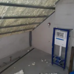 Poddasze w trakcie adaptacji, widoczne ocieplenie pianą, stelaż podtynkowy WC z niebieską ramą i instalacje elektryczne w ścianie.