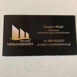 WUJEK NIERUCHOMOŚCI - Wizytówka pośrednika nieruchomości Grzegorza Wujka z logo przedstawiającym budynki. Czarno-złota kolorystyka, wyraźny numer telefonu i adres e-mail.
