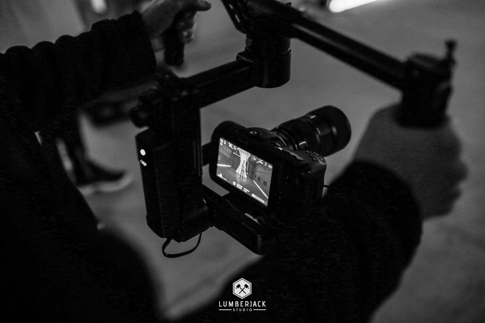 Kamera na stabilizatorze, na ekranie widoczna postać w jasnym pomieszczeniu, logo Lumberjack Studio w dolnej części kadru.