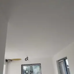 Wnętrze po remoncie, świeżo pomalowane ściany i sufit na biało, widoczne okna PCV i wystające kable elektryczne.