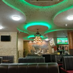 Usługi remontowe RJ - Wnętrze lokalu gastronomicznego z dekoracyjnym sufitem podwieszanym z zielonym oświetleniem LED, wiszącą lampą w stylu orientalnym i muralem na ścianie.