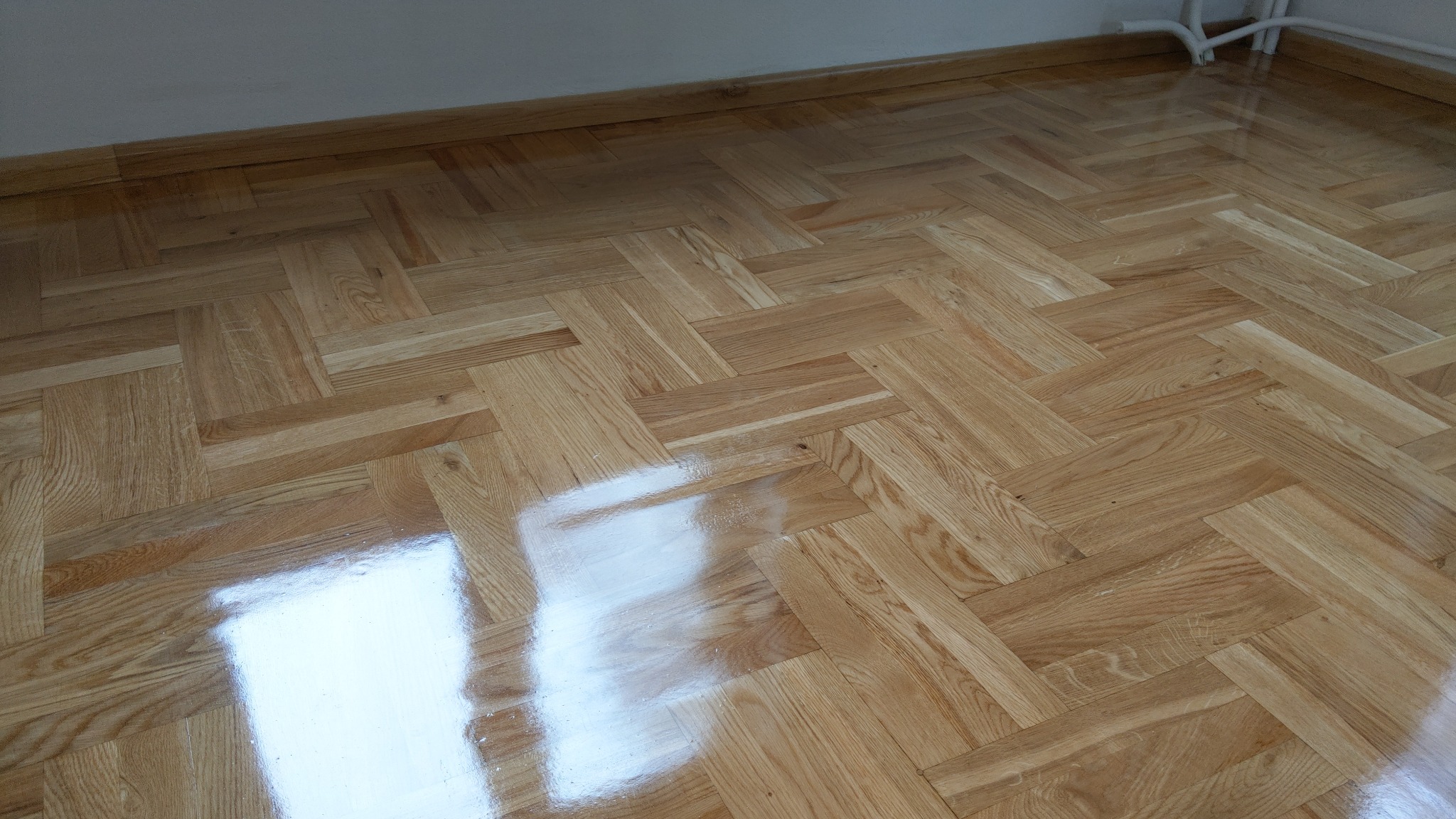 Parkiet ułożony w jodełkę, świeżo po lakierowaniu, z widocznym odbiciem światła.