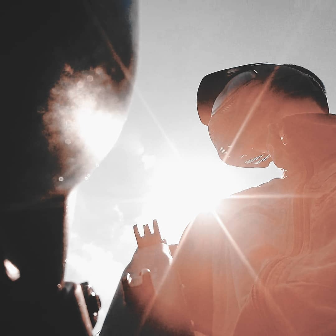 Uczestnicy rozgrywki paintball w pełnym ekwipunku ochronnym, silne światło słoneczne w tle.