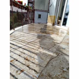 Błyszcząca, marmurkowa terakota na balkonie z metalową balustradą, cień rzucany przez balustradę, widoczne kwiaty w doniczkach.