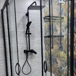 Nowoczesna kabina prysznicowa z czarnymi profilami i deszczownicą na tle białej ściany z falistą strukturą oraz ściany z motywem tropikalnych liści.