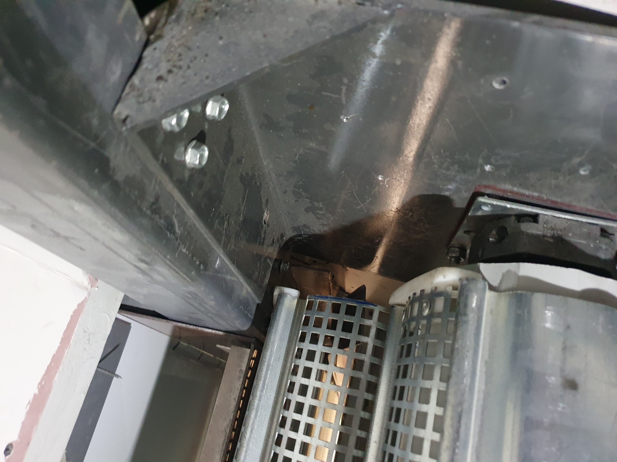 Widok od dołu na mechanizm rolety zewnętrznej, z widocznymi śrubami mocującymi i metalową konstrukcją.