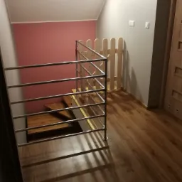 Klatka schodowa z drewnianymi schodami, metalową balustradą i zabezpieczeniem dla dzieci w postaci drewnianego płotka.