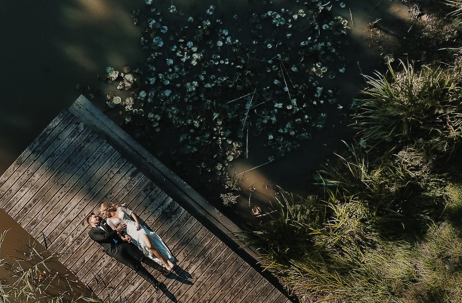 Para młoda leżąca na drewnianym pomoście nad jeziorem z liliami wodnymi, widok z góry.